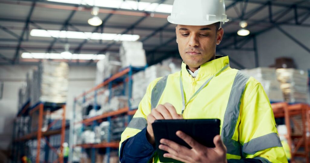 Técnico de manutenção industrial usa tablet em armazém, simbolizando checklist para produtividade contínua.